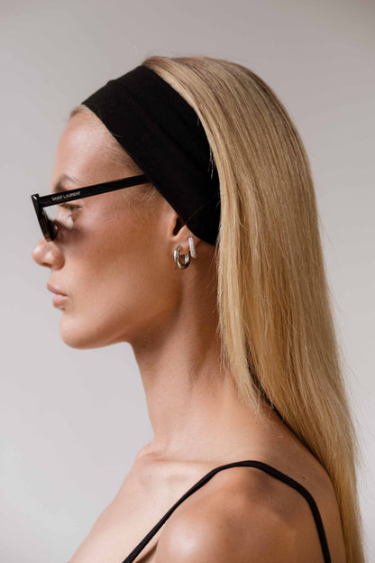 Profile of a woman with long blonde hair wearing a black headband, stylish sunglasses, and silver hoop earrings. Fashion accessories, modern style.