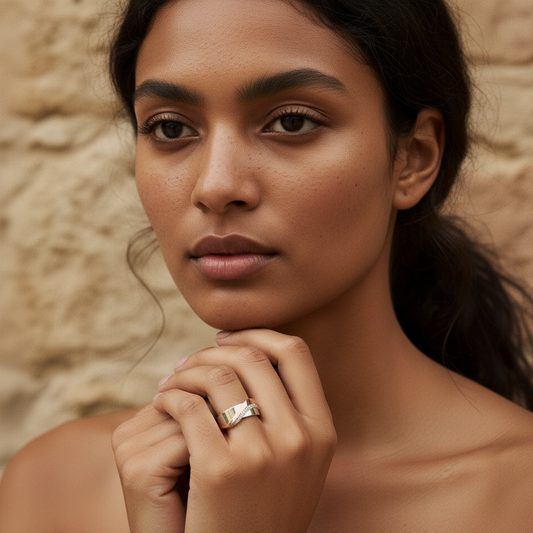 A woman with long hair wearing a silver ring poses against a stone wall, showcasing natural beauty and elegant jewelry.