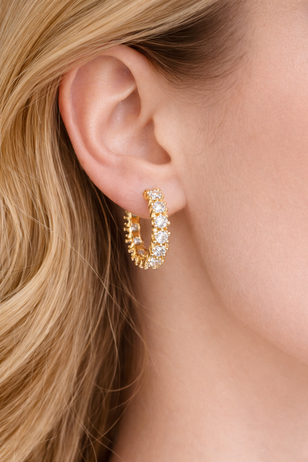 Gold hoop earrings with clear stones worn by a person with blonde hair.