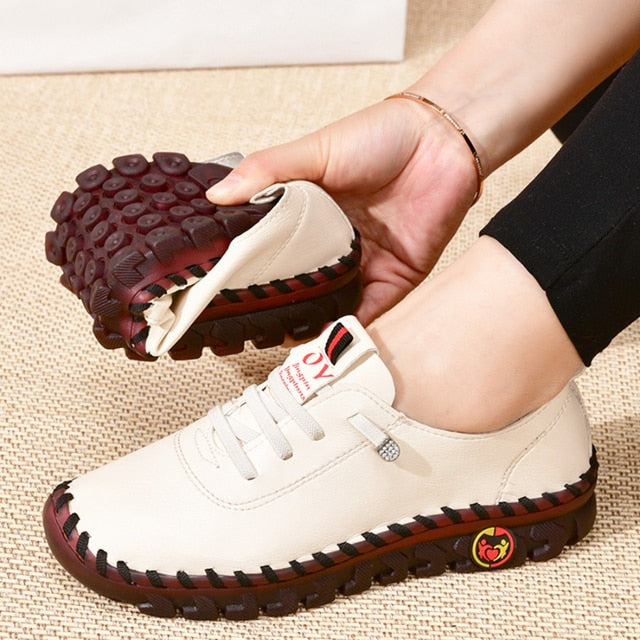 White sneakers with red soles held by a hand on a textured surface