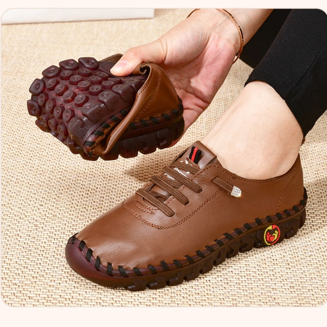 Brown leather shoe with textured sole held by a hand on a beige fabric background