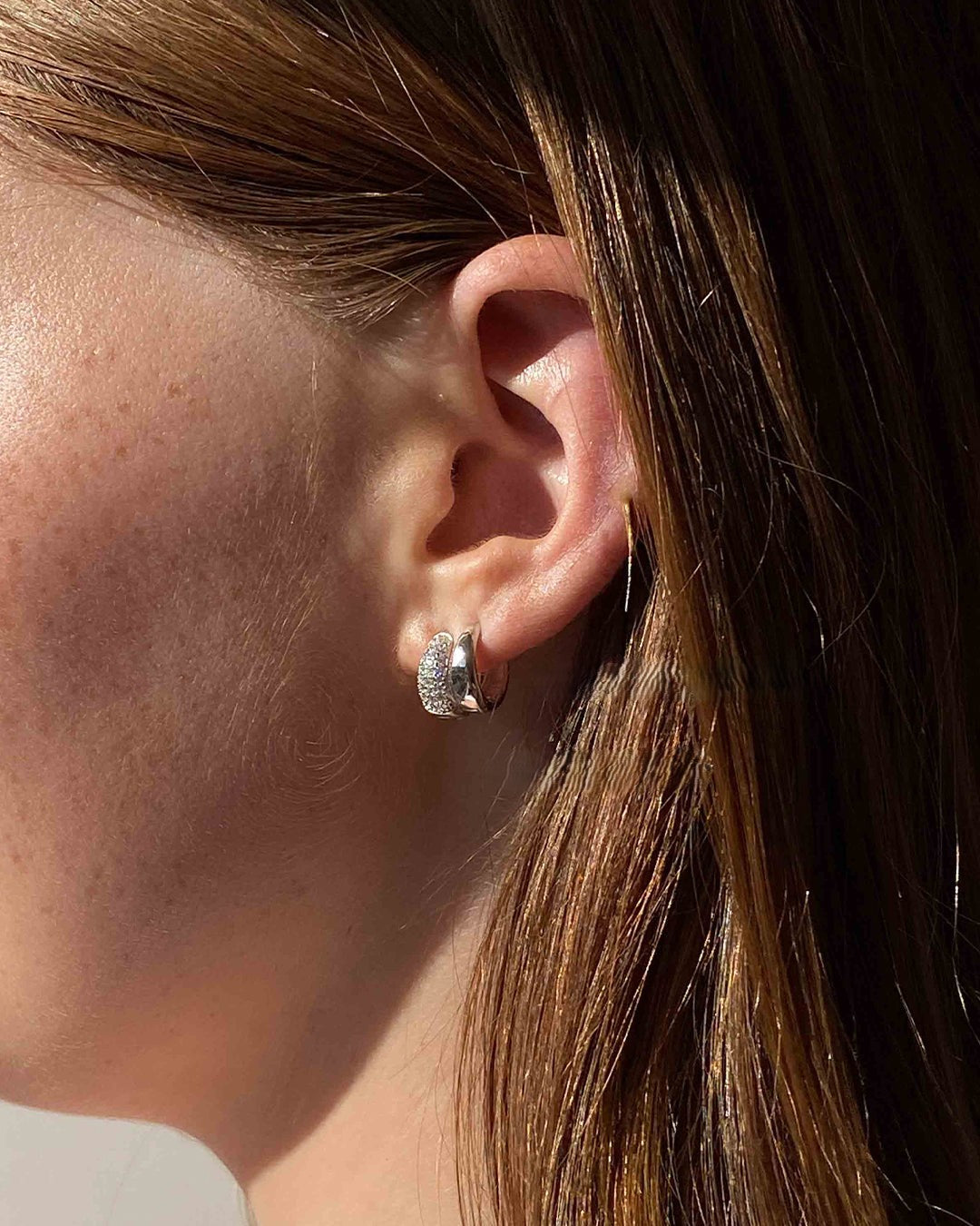 Close-up of an ear wearing a silver hoop earring with hair partially covering the face.