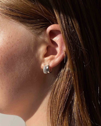 Close-up of an ear wearing a silver hoop earring with hair partially covering the face.