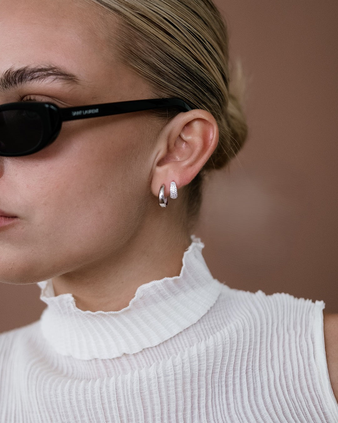 Close-up of a person wearing black sunglasses and a white sleeveless top with a blurred background
