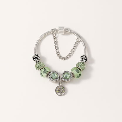 Silver charm bracelet with green beads and intricate designs, featuring a tree of life pendant. Elegant jewelry accessory, perfect for fashion enthusiasts.