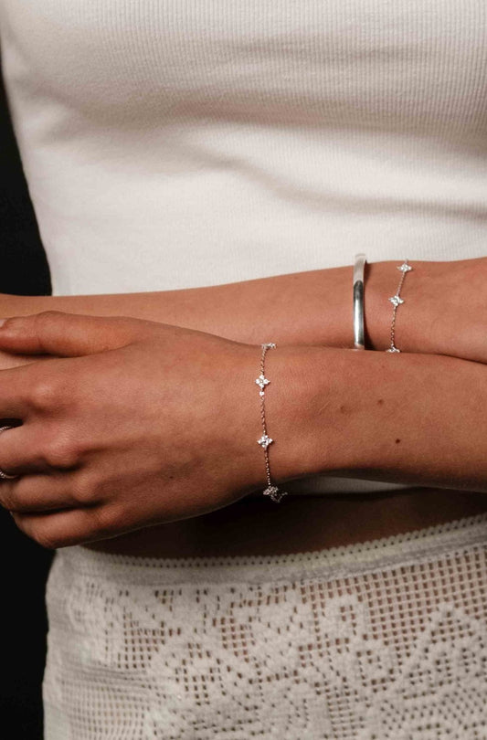 Close-up of a person's arm wearing two silver bracelet sets against a neutral background.