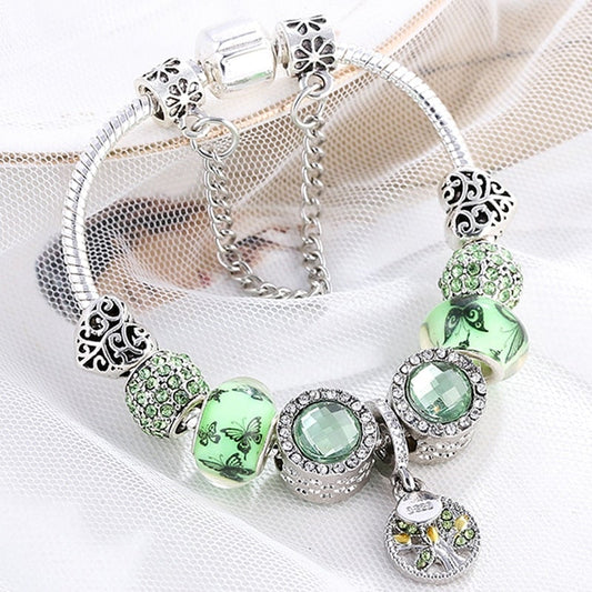 Silver charm bracelet with green crystal beads, butterfly designs, and intricate heart-shaped charms on a delicate chain. Fashion jewelry accessory.