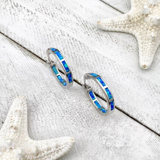 Silver hoop earrings with blue opal inlay on a white wooden surface, adorned with starfish. Elegant beach-themed jewelry.