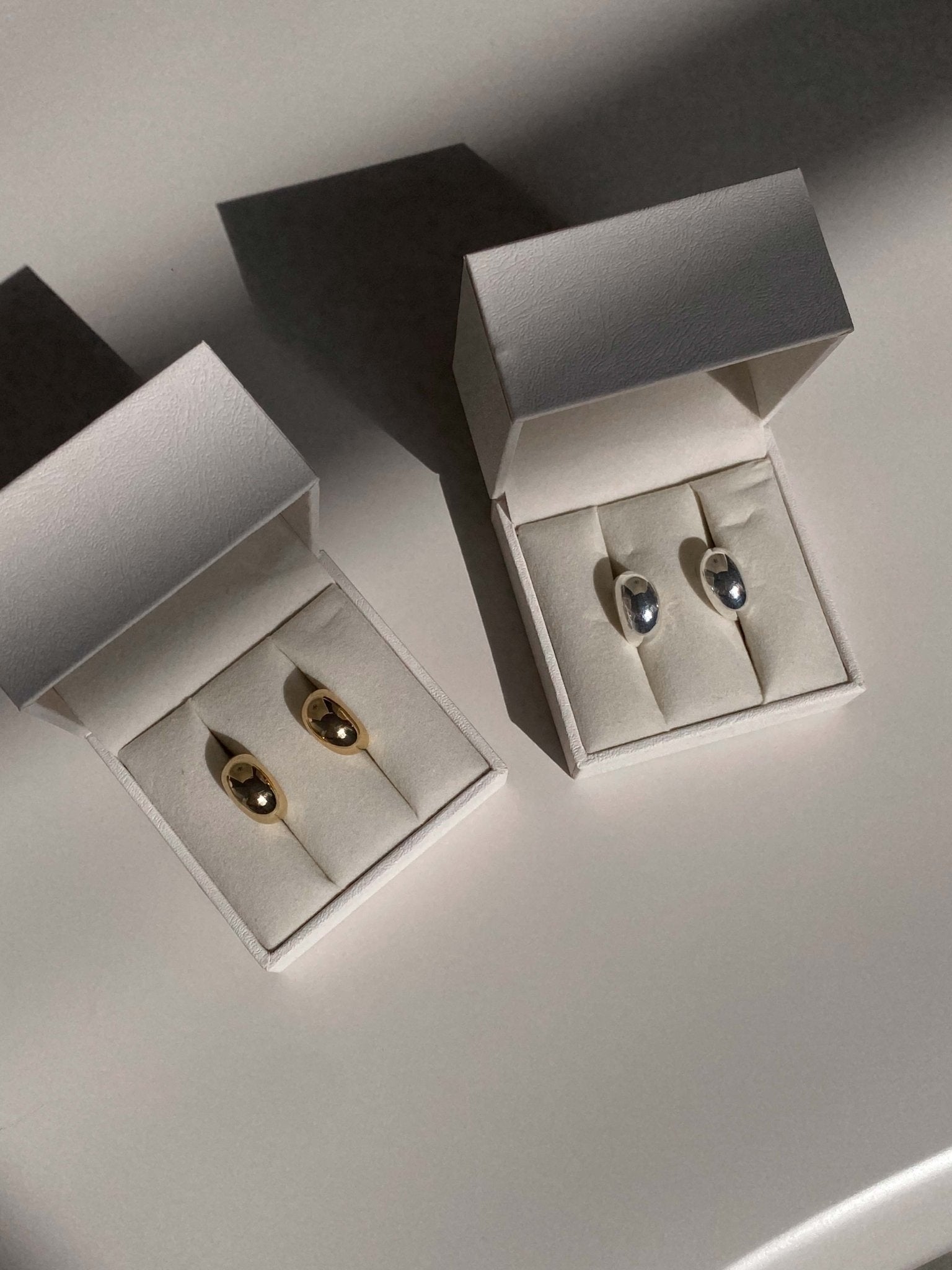 Gold and silver hoop earrings in elegant white jewelry boxes, displayed on a soft beige surface. Perfect for fashion accessories and gift ideas.