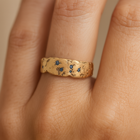 Gold ring with blue stones on a finger against a neutral background