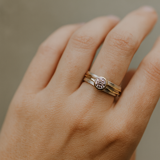 Hand wearing a gold ring with a circular design on a neutral background