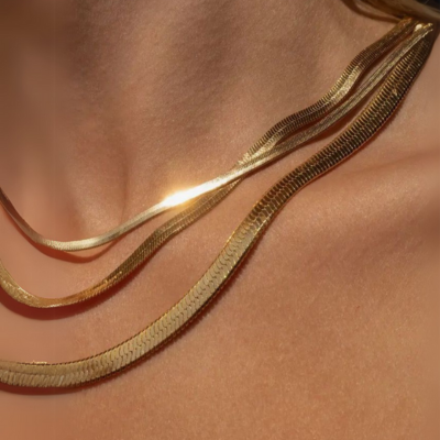 Close-up of a woman's neck adorned with layered gold snake chain necklaces, reflecting light. Elegant jewelry fashion, luxury accessories.
