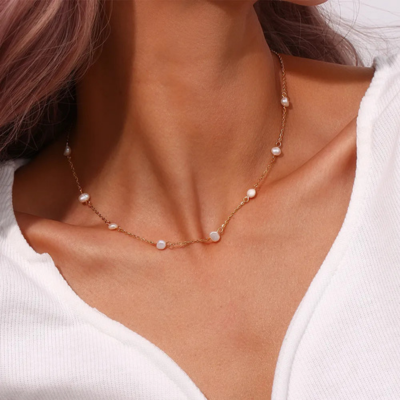 Woman wearing a delicate gold chain necklace with small pearls, paired with a white V-neck top. Elegant jewelry fashion accessory.