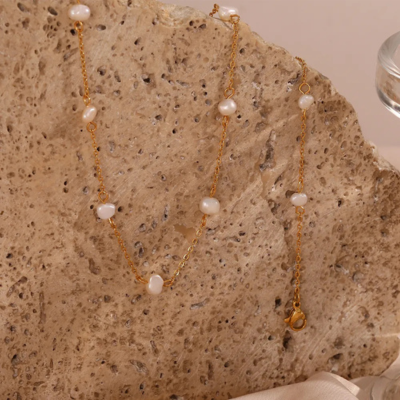 Gold chain necklace with white pearls on textured stone background, elegant jewelry, minimalist design, fashion accessory, luxury style.