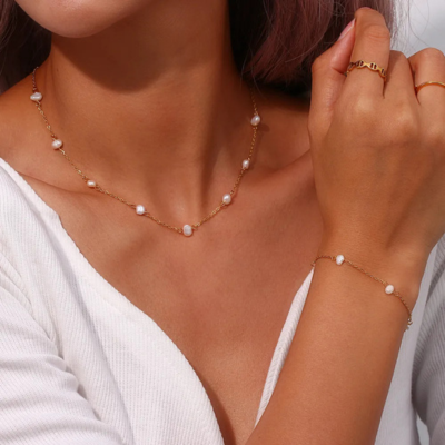 Woman wearing a gold chain necklace and bracelet with pearls, paired with a white top. Elegant jewelry fashion, pearl accessories, gold jewelry.
