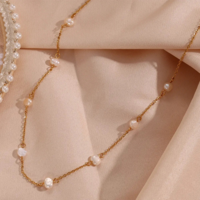 Elegant gold chain necklace with pearls on a soft beige fabric background, showcasing luxury jewelry design and fashion accessory trends.