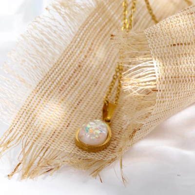 Opal pendant necklace with gold chain on textured beige fabric, showcasing iridescent gemstone. Elegant jewelry, luxury fashion accessory.