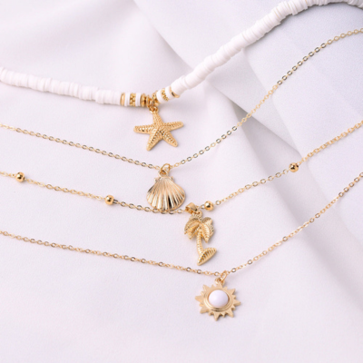 Gold layered necklaces with starfish, shell, palm tree, and sun pendants on white fabric. Elegant beach-themed jewelry, perfect for summer fashion.