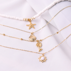 Gold layered necklaces with starfish, shell, palm tree, and sun pendants on white fabric. Elegant beach-themed jewelry, perfect for summer fashion.