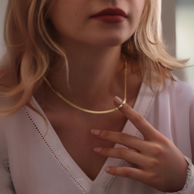Woman wearing a gold necklace and white blouse, gently touching the jewelry. Elegant fashion accessory, minimalist style, close-up.