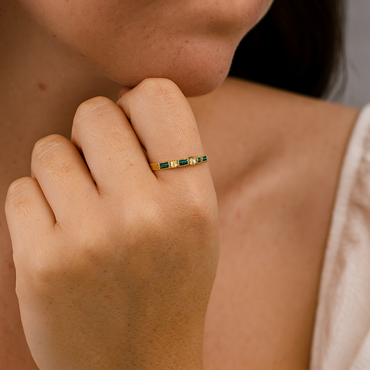 Close-up of a hand wearing a gold ring with green gemstones.