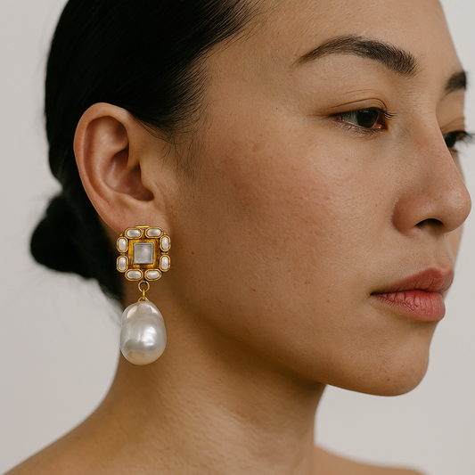 Close-up of a woman wearing a pearl earring with a gold frame against a neutral background