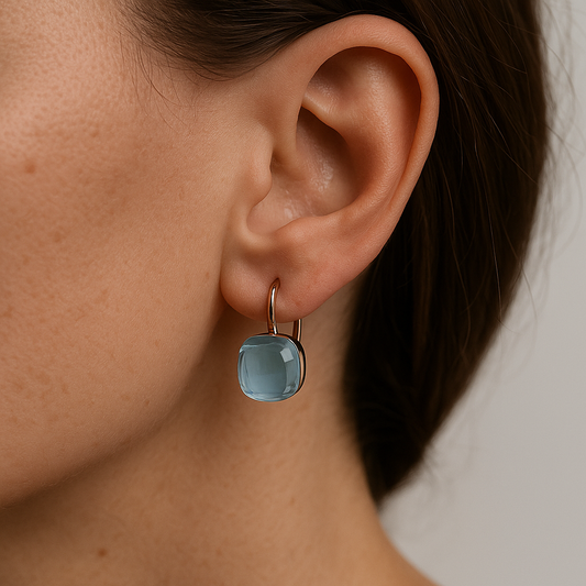 Close-up of an ear wearing a blue earring with a neutral background