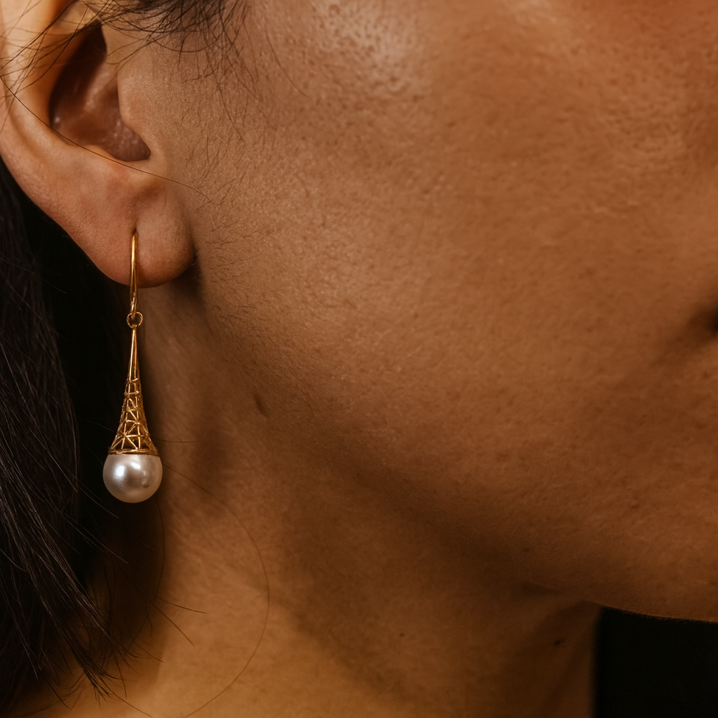 Close-up of a person wearing a gold earring with a pearl drop.