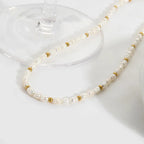 Pearl and gold beaded necklace draped over a glass on a white surface