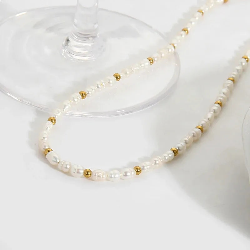 Pearl and gold beaded necklace draped over a glass on a white surface