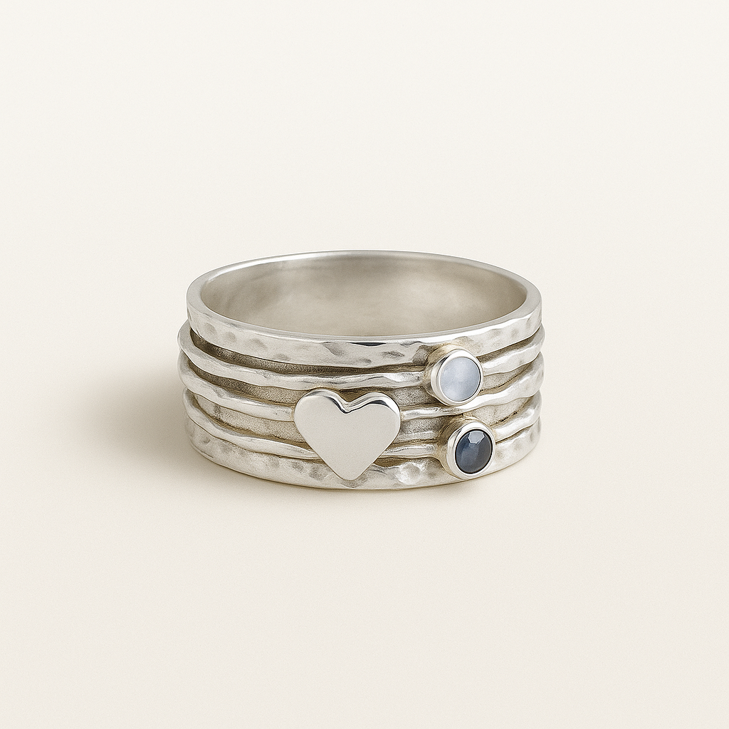 Stack of silver rings with heart and gemstone designs on a light background