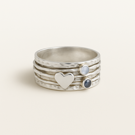 Stack of silver rings with heart and gemstone designs on a light background