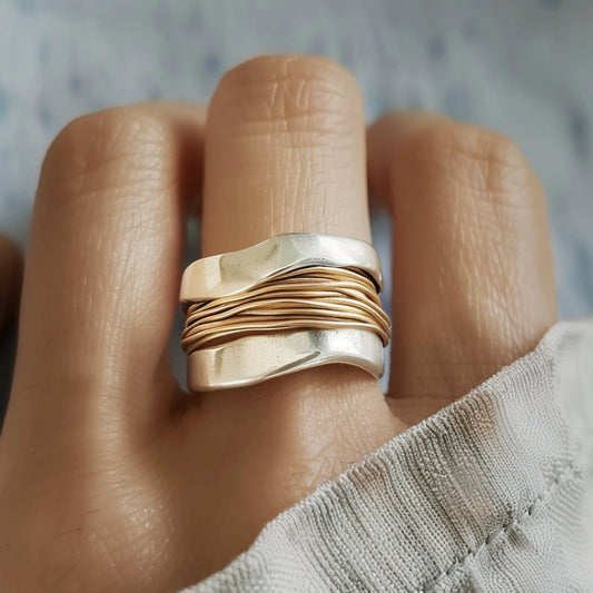 Silver and gold wave ring on finger, featuring intertwined metal bands. Unique, handcrafted jewelry design, perfect for fashion and style enthusiasts.