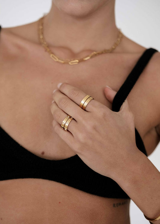 Woman wearing gold rings and a chain necklace, dressed in a black top. Fashion jewelry, minimalist style, close-up on accessories.