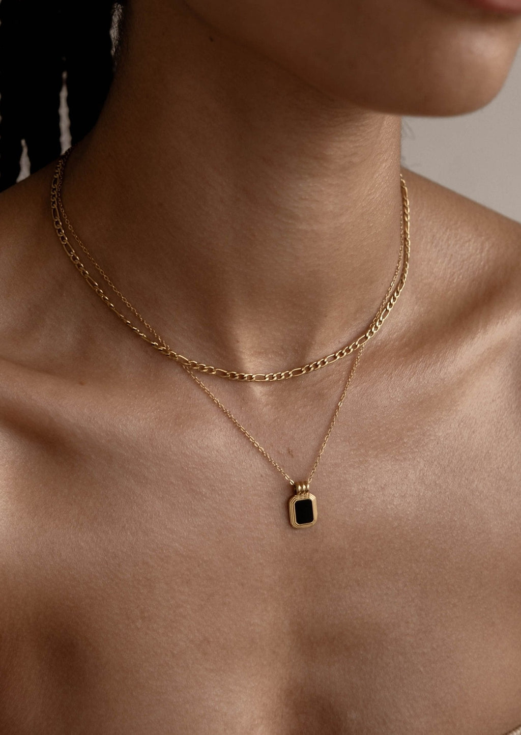 Gold layered necklaces with a black pendant on a woman's neck, showcasing elegant jewelry fashion. Perfect for style and accessory enthusiasts.