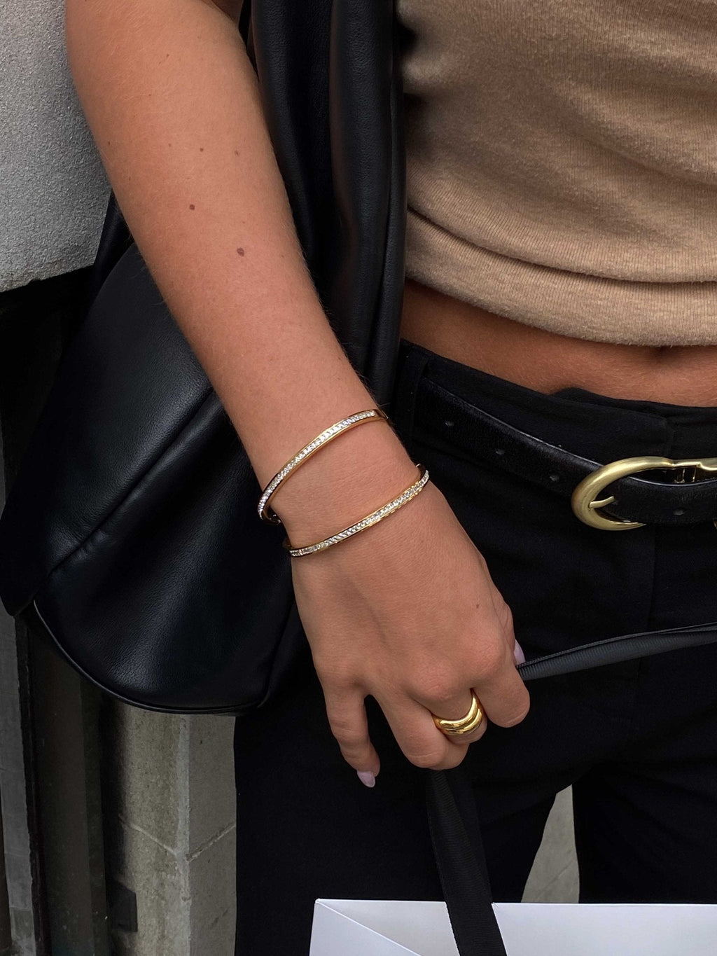 Woman wearing gold bangles and rings, holding a black leather bag. Fashionable accessories, stylish outfit, elegant jewelry, chic look.