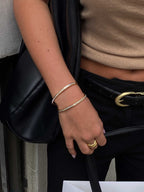 Woman wearing gold bangles and rings, holding a black leather bag. Fashionable accessories, stylish outfit, elegant jewelry, chic look.
