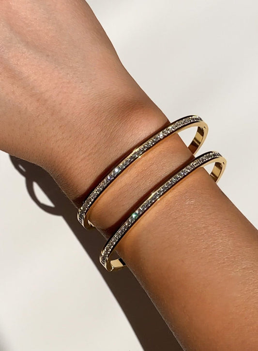 Gold bangles with embedded diamonds on a wrist, sparkling in sunlight. Elegant jewelry, luxury fashion accessory, perfect for special occasions.