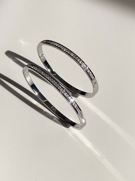 Elegant silver bangles with embedded diamonds, casting shadows on a white surface. Luxurious jewelry, sparkling diamond bracelets, fashion accessory.