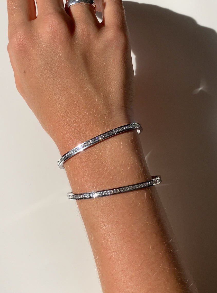 Elegant silver bangles with embedded diamonds on a wrist, sparkling under natural light. Luxury jewelry, diamond bracelets, fashion accessories.