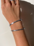 Elegant silver bangles with embedded diamonds on a wrist, sparkling under natural light. Luxury jewelry, diamond bracelets, fashion accessories.