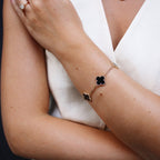 Elegant woman wearing a gold bracelet with black four-leaf clover charms, paired with a diamond ring, showcasing luxury fashion accessories.