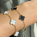 Elegant gold bracelet with black and white clover-shaped charms on wrist, luxury jewelry, fashion accessory, stylish design, close-up.