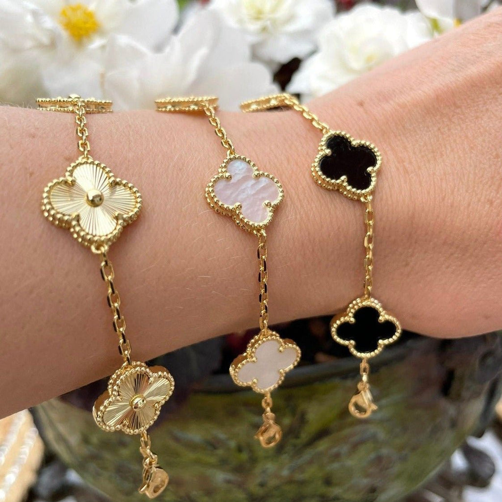 Gold clover bracelets on wrist, featuring floral designs with black, white, and pink accents. Elegant jewelry, luxury fashion accessory.