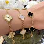 Gold clover bracelets on wrist, featuring floral designs with black, white, and pink accents. Elegant jewelry, luxury fashion accessory.