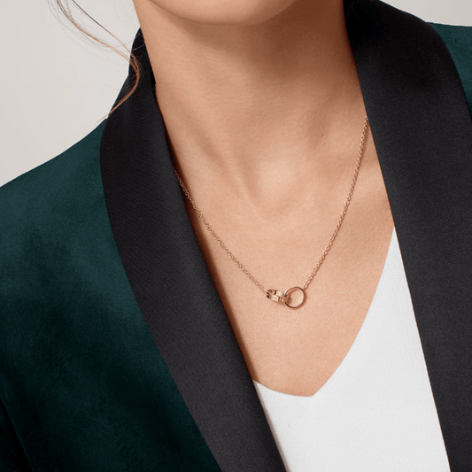 Woman wearing elegant rose gold necklace with interlocking rings, paired with a dark green blazer and white top. Fashion jewelry accessory.