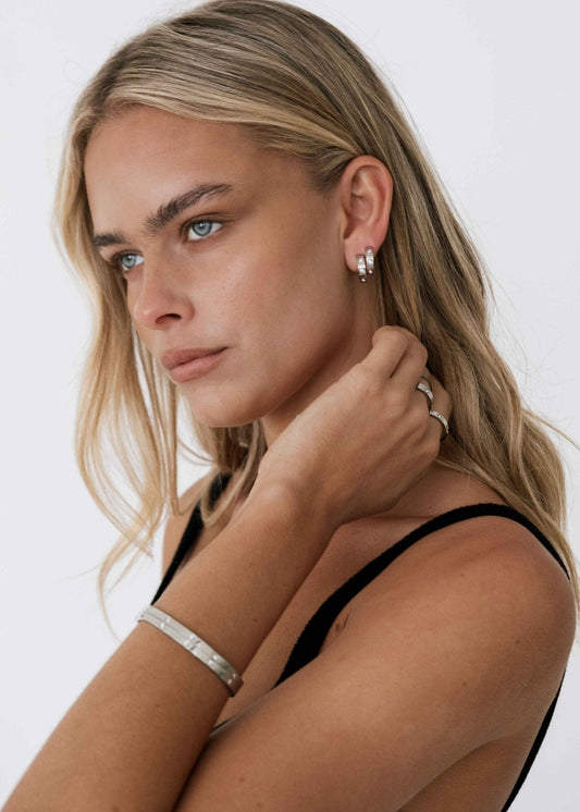 Blonde woman wearing silver hoop earrings and a matching bracelet, gazing sideways. Fashion jewelry, minimalist style, elegant accessories.