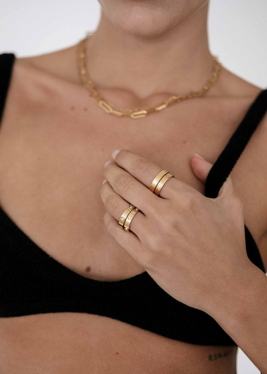Woman wearing gold rings and a chain necklace, dressed in a black top. Fashion jewelry, minimalist style, elegant accessories.