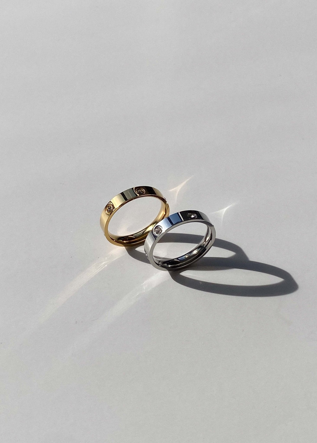 Two elegant gold and silver rings with small diamonds on a smooth white surface, casting soft shadows; luxury jewelry, minimalist design.