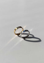 Two elegant gold and silver rings with small diamonds on a smooth white surface, casting soft shadows; luxury jewelry, minimalist design.